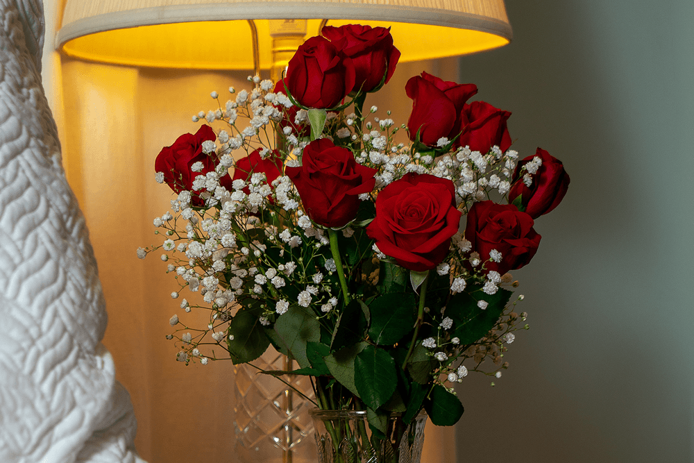 A bouquet of red roses with white baby's breath beside a lamp.