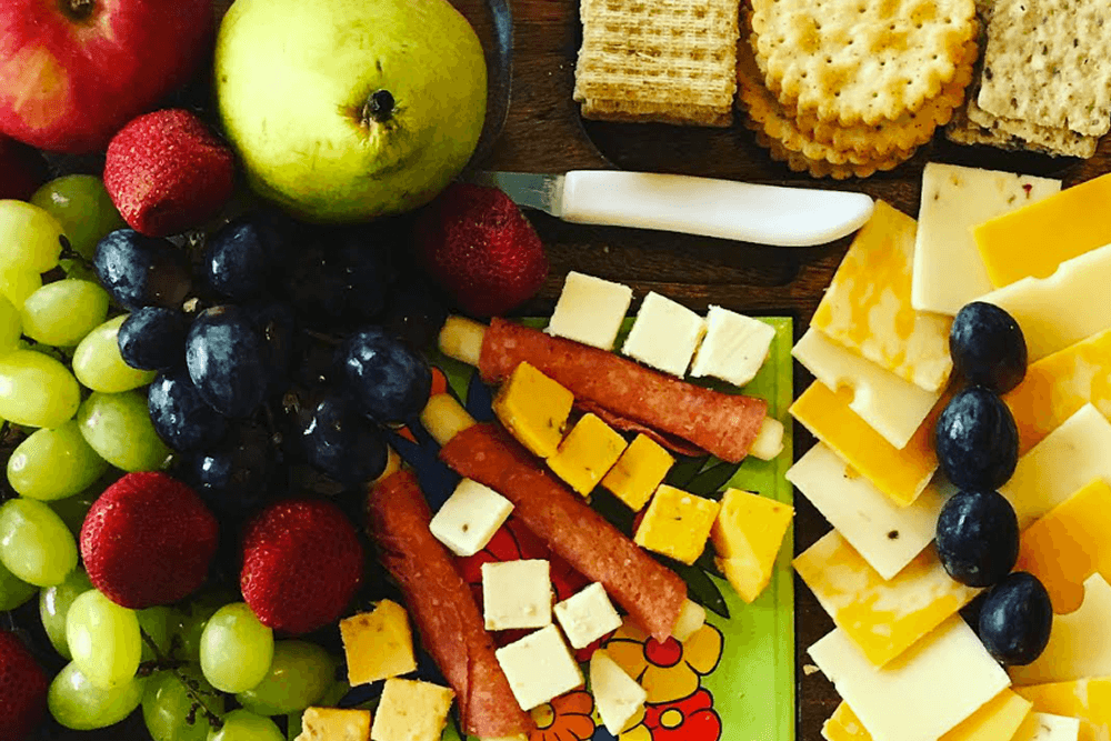 A colorful assortment of fruits, cheeses, and crackers arranged on a wooden board.