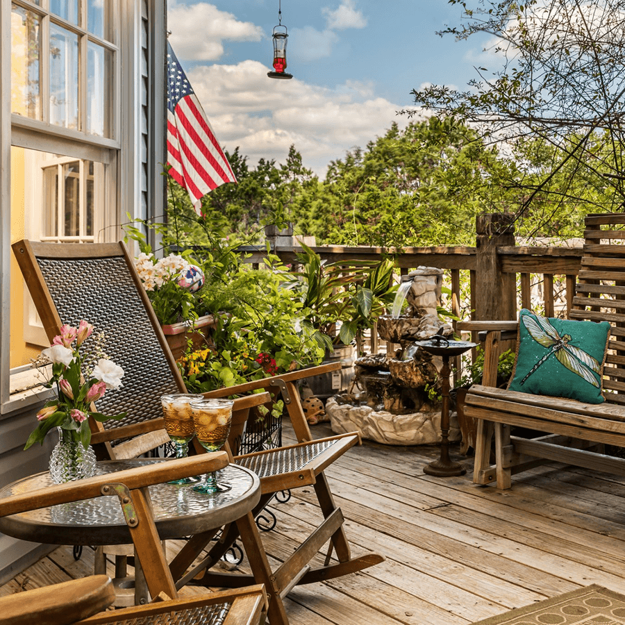 A cozy porch adorned with plants, a flag, and drinks on a table.