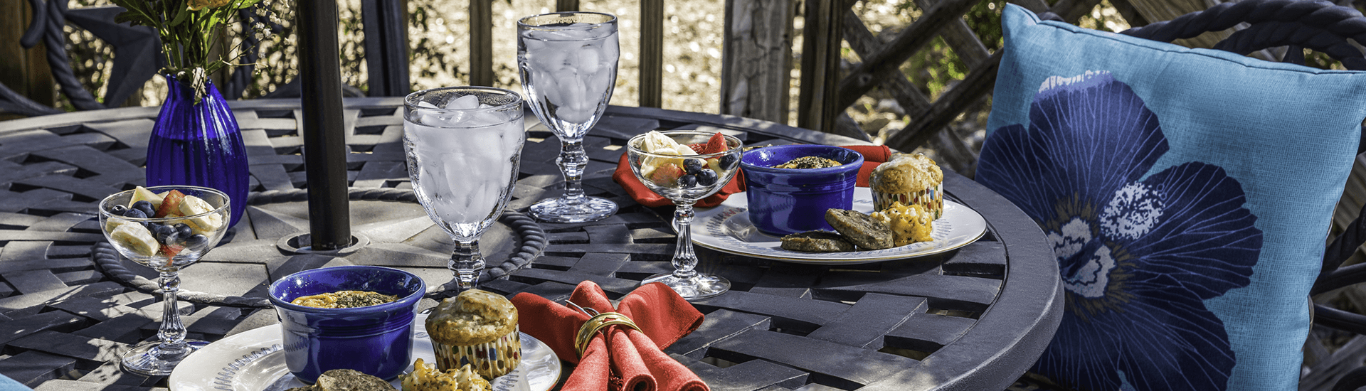 A table set with drinks, colorful fruit, and baked goods, surrounded by a vibrant outdoor setting.