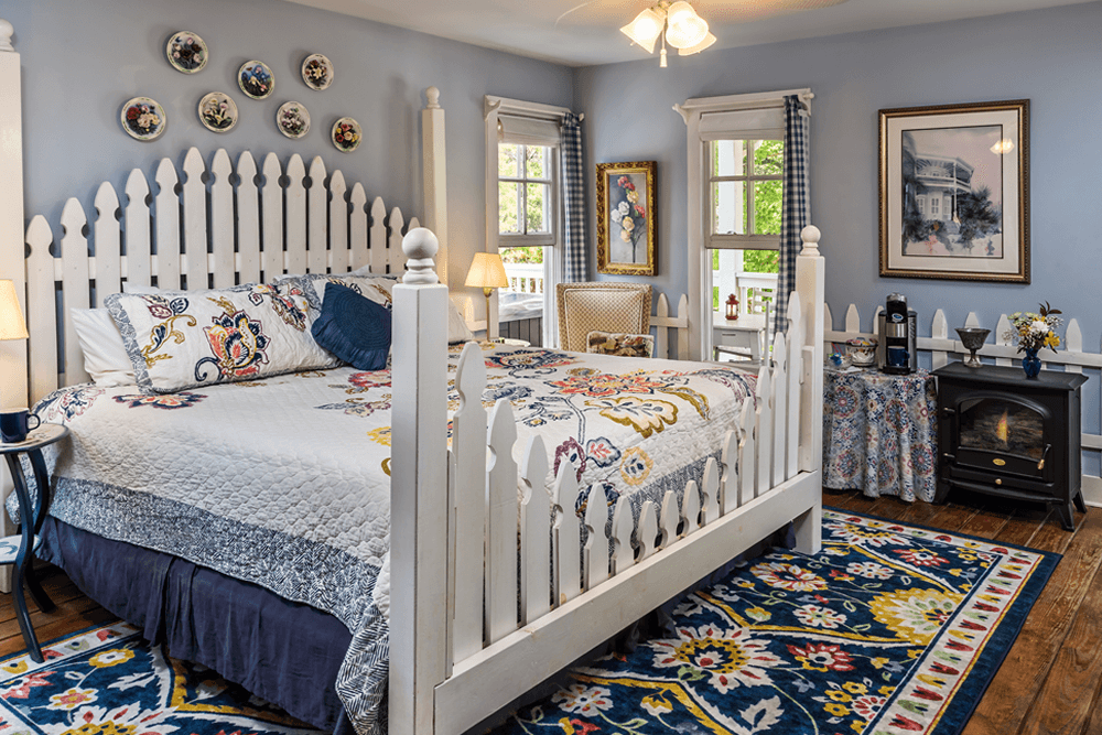 A cozy, stylish bedroom featuring a white picket fence headboard, floral bedding, and colorful patterned rug.