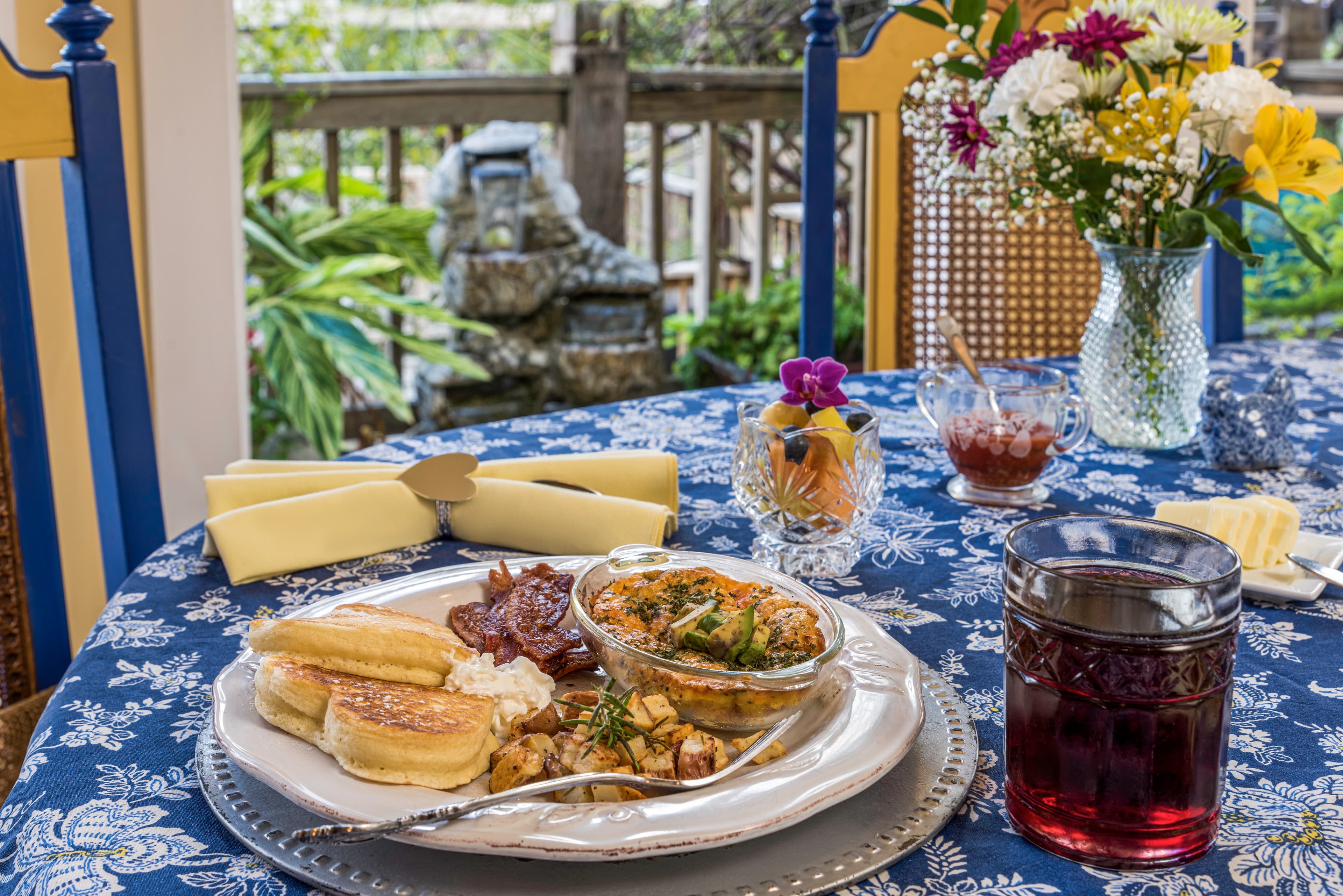 A beautifully arranged breakfast plate featuring pancakes, a savory casserole, and a glass of iced tea on a floral tablecloth.